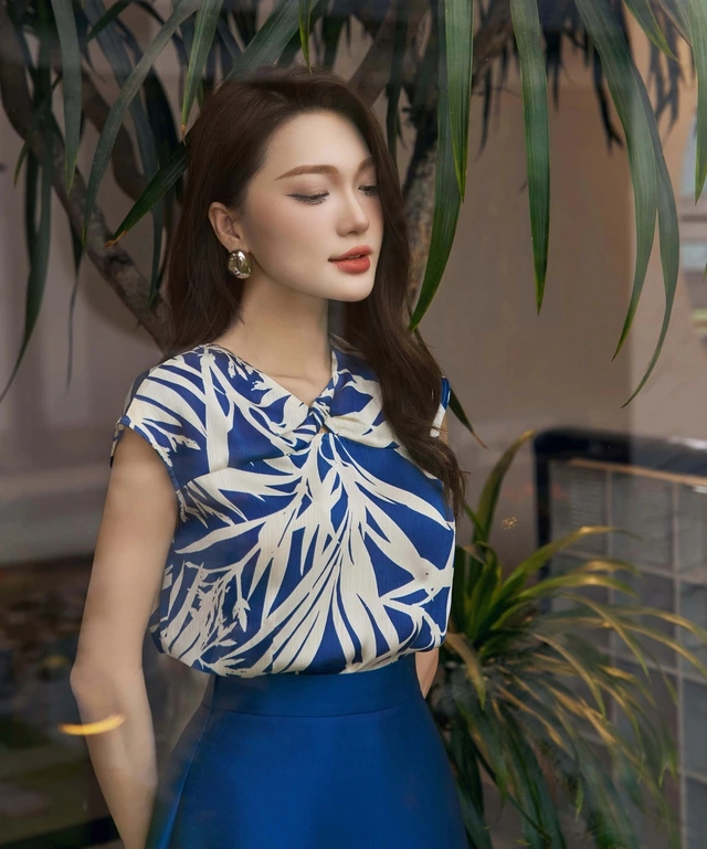 Áo cách điệu kết hợp hoàn hảo giữa nét cổ điển và hiện đại qua màu nền họa tiết, chi tiết vặn xoắn độc đáo phối cùng chân váy dài màu xanh nước biển
