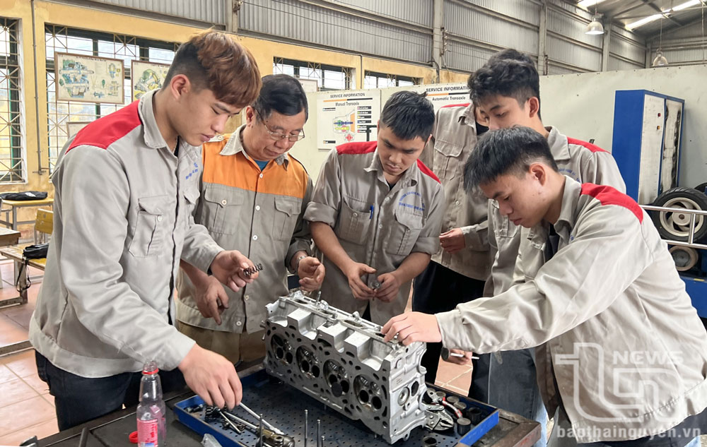 Giáo viên hướng dẫn học sinh lớp trung cấp nghề ô tô thực hành sửa chữa động cơ.